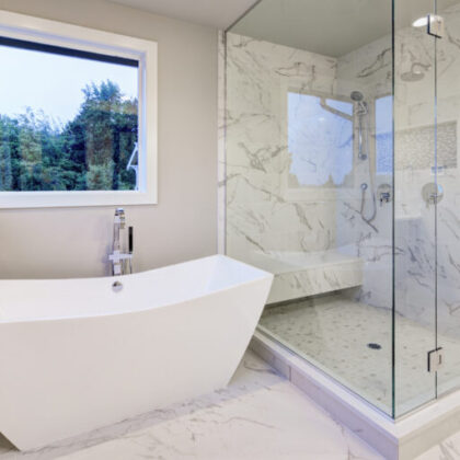 Sleek bathroom features freestanding bathtub atop marble floor placed in front of glass shower accented with rain shower head and gray and white marble surround. Northwest, USA