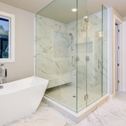 Sleek bathroom features freestanding bathtub atop marble floor placed in front of glass shower accented with rain shower head and gray and white marble surround. Northwest, USA