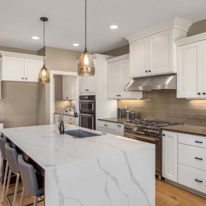 Kitchen in new luxury home with waterfall isalnd, stainless steel appliances, pendant lights, and hardwood floors